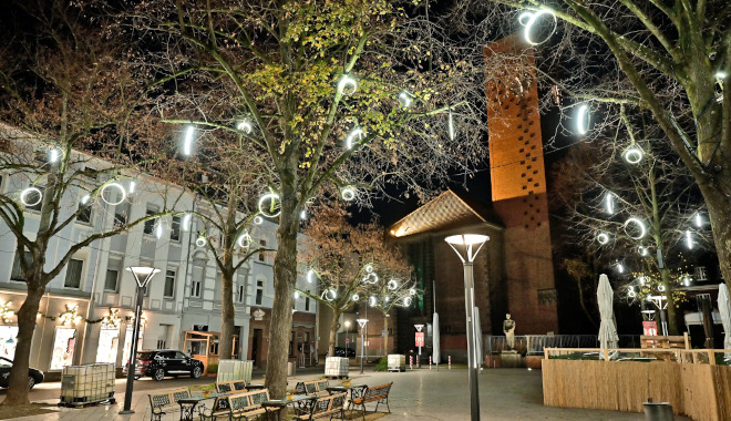 Die Lichtringe in den Bäumen erhellen den Platz an der alten Kirche.